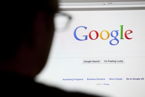 Close up of Google.com search home page on computer with silhouette of man's head out of focus in foreground