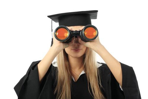A woman in a cap and gown looks through binoculars