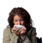Middle aged, woman sick with flu sneezes into a tissue