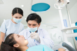 Dentist working on patient, as intern looks on