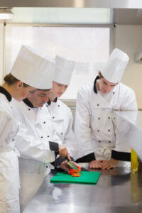 Culinary students being taught how to chop vegetables in a kitchen
