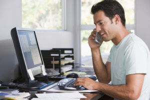 Man working from home in office, using computer and telephone