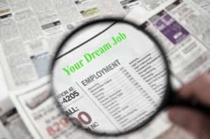 Magnifying glass over classified section of newspaper, searching dream job