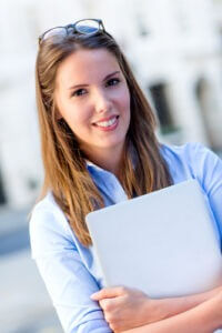 Smiling female intern holding a laptop outdoors