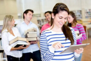 Woman using e-reader while friends carry books in the background