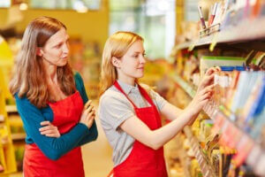 Intern organizing shelves in supermarket under supervision of store manager