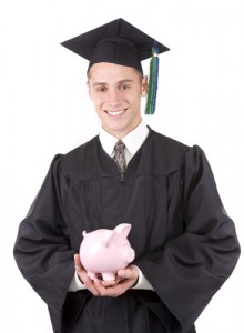Young male graduate in cap and gown holding piggy bank