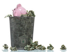 Garbage can full of money spilling over with piggy bank in it and money on the ground