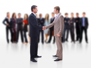 Two men shaking hands with people in the background (business)