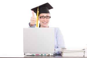Woman with graduation cap using laptop with thumbs up; online education