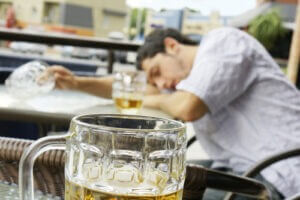Alcohol abuse: drunk young man or student lying down on a table with beer bock still in hand, focus on glass up front. 