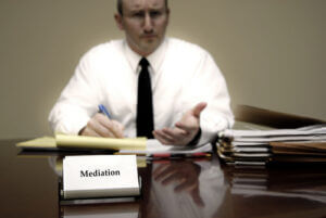 Attorney at law sitting at desk holding pen with files with a card for Mediation