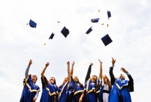 Image of happy young graduates throwing hats in the air