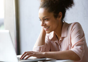 Close up portrait of a young woman smiling and looking at laptop screen
