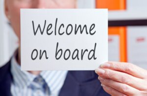 Welcome on board - businesswoman holding white sign with text in the office courtesy of Shutterstock.com